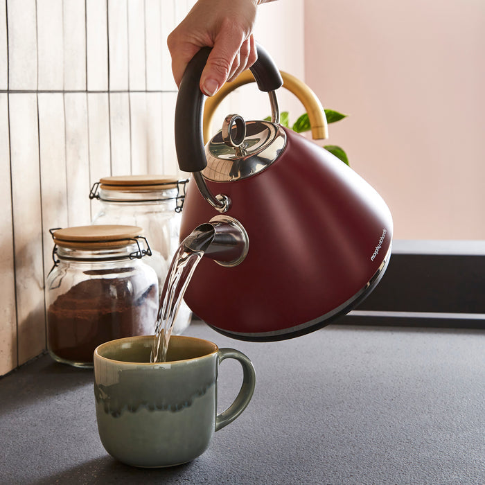 Red kettle pouring water into a green mug on a kitchen counter.