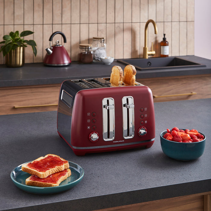 Red toaster with slices of bread and a bowl of fruit on a kitchen counter.