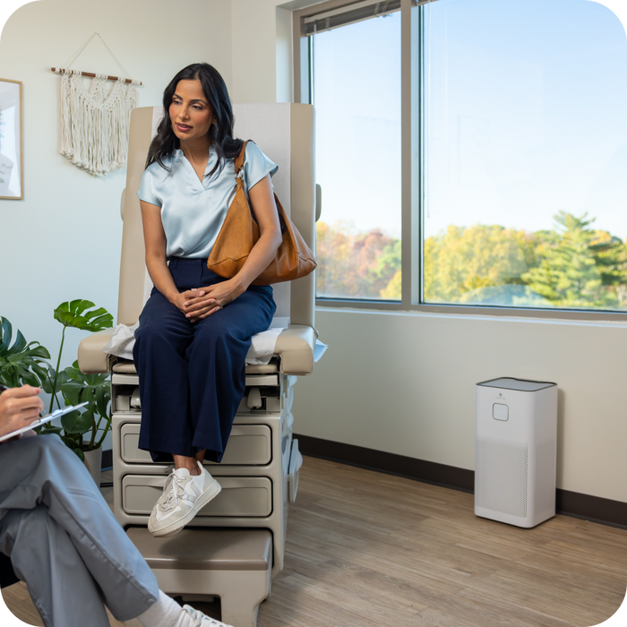 a female sitting on Family Practice Exam Table next to a window and an air purifier talking to a practitioner.