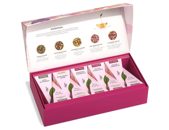 Pink gift box containing six white tea sachets labeled with different flavors and dried tea blend samples displayed in lid.