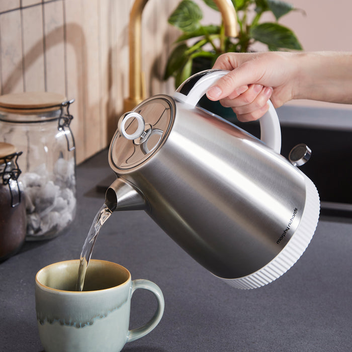 Stainless steel electric kettle being used to pour water into a mug on a kitchen counter.