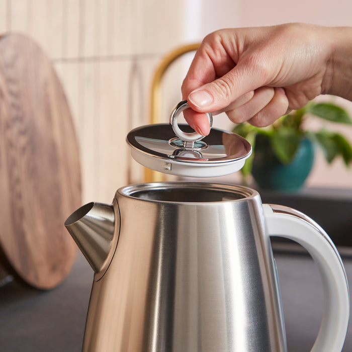 Hand opening a silver electric kettle with a blurred kitchen background