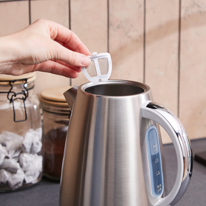 Stainless steel kettle with digital display being held by a hand in a kitchen setting.