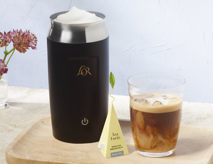 MAIN PDP | Black milk frother with a glass of iced coffee and a tea bag on a wooden board.