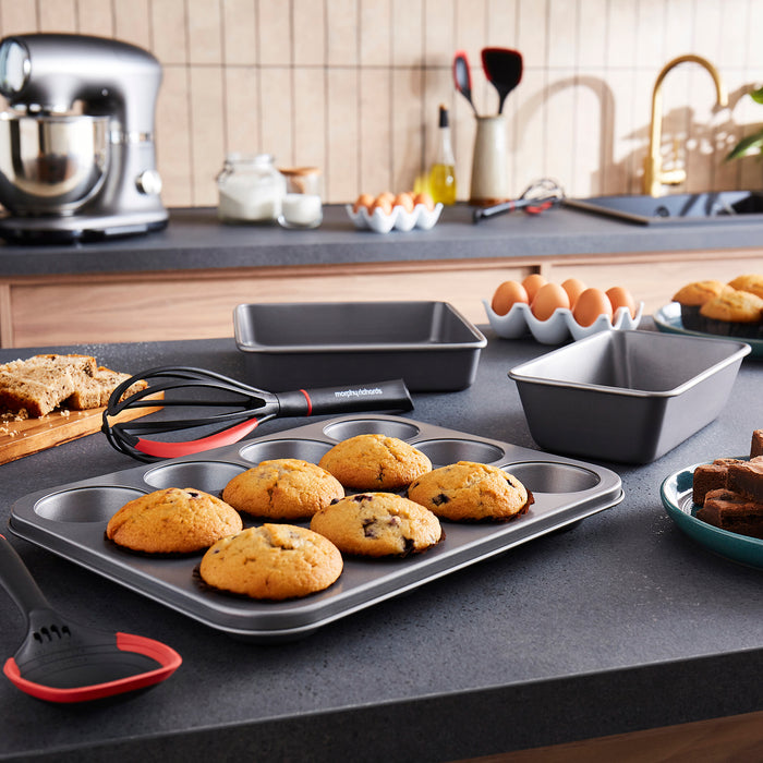 Baked cookies on a muffin tray with kitchen utensils and ingredients in the background