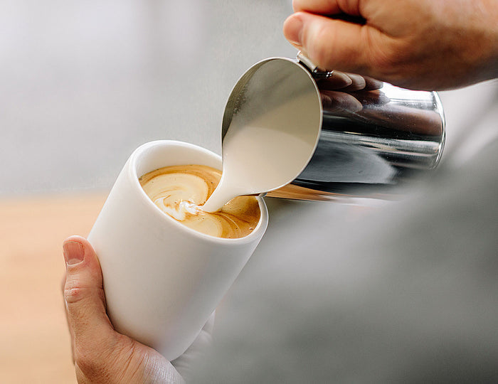 Pouring steamed milk into a Monty Milk Cup with coffee already inside
