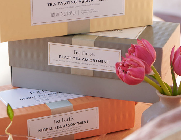 MAIN PDP |  Black Tea Assortment Presentation Box of 20 infusers, with other boxes stacked and tulips