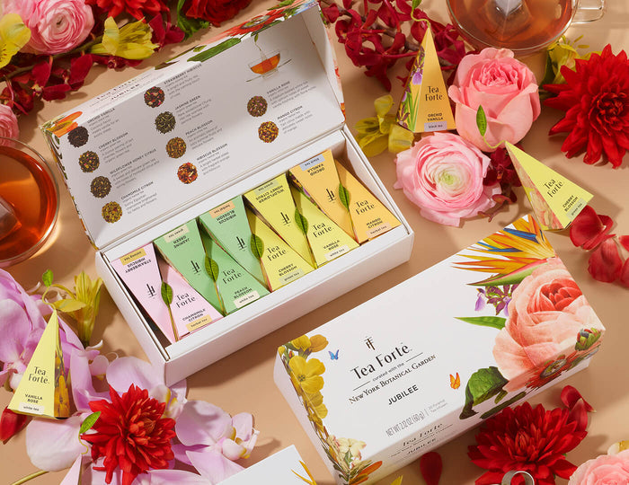 MAIN PDP | Jubilee Presentation Box of 20 pyramid infusers, open and closed, on a table filled with flowers and pyramid tea infusers