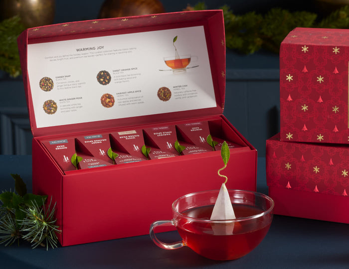MAIN PDP | Presentation Box Warming Joy open and a glass cup of tea on a dark blue background