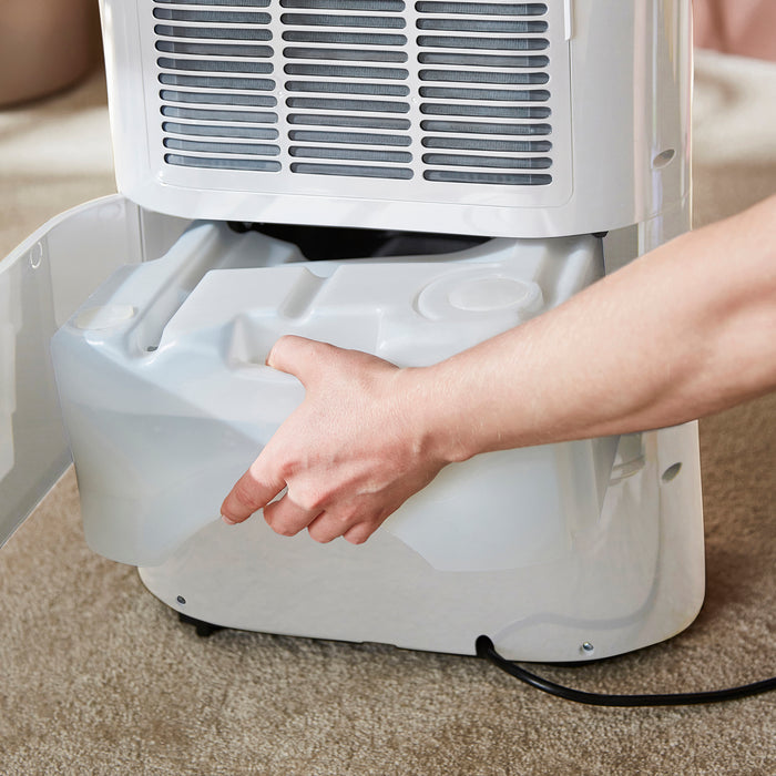 Person replacing a water tank in a dehumidifier on a carpeted floor.