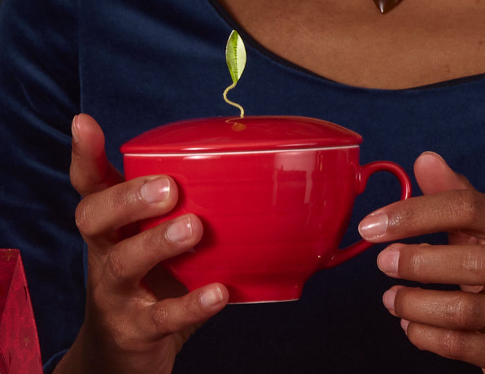 MAIN PDP | Ruby Red café Cup being hand in someone hands with lid on and tea inside