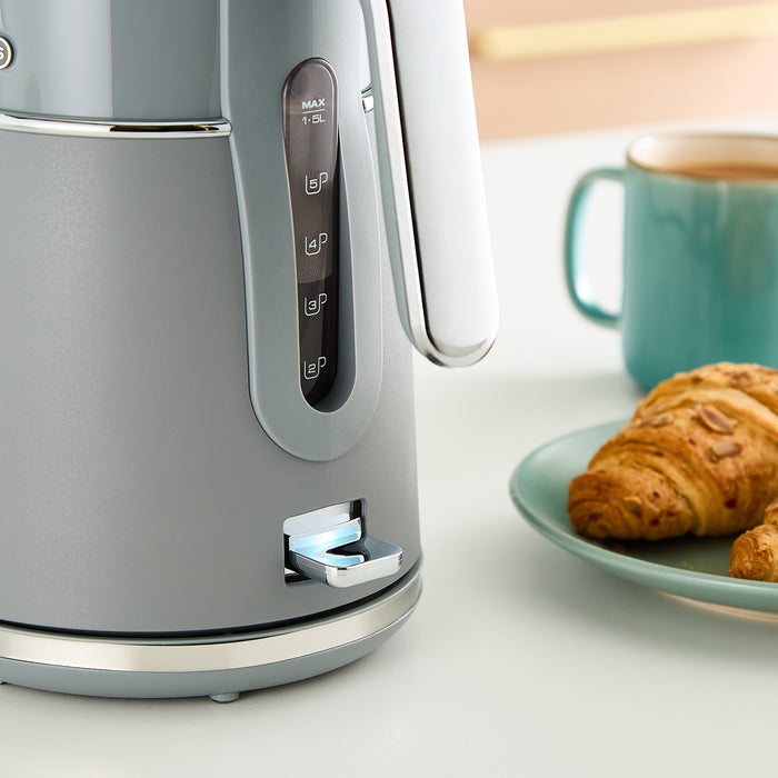 Grey kettle on a white surface with a croissant and mug in the background