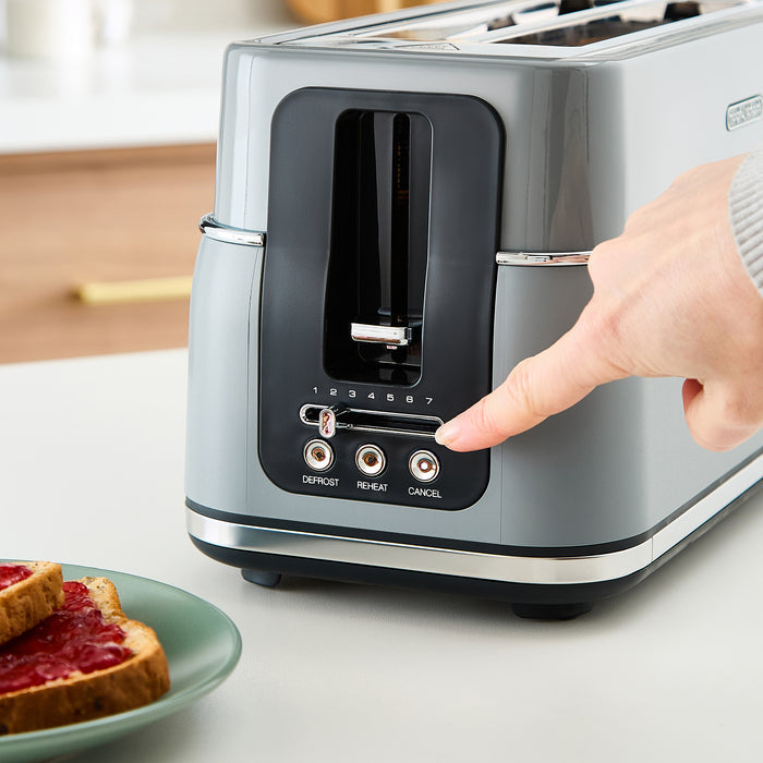 Person using a grey toaster with a plate of toast and jelly on a kitchen counter.