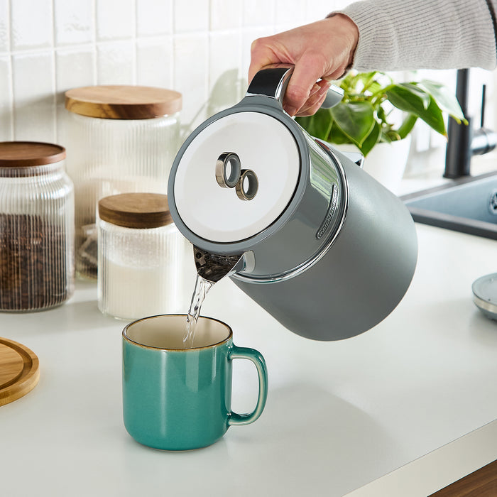 Person pouring water from a grey kettle into a teal mug on a kitchen counter.