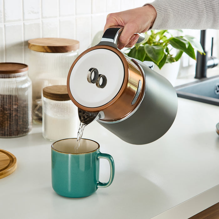 Person pouring water from a grey kettle into a teal mug on a kitchen counter.