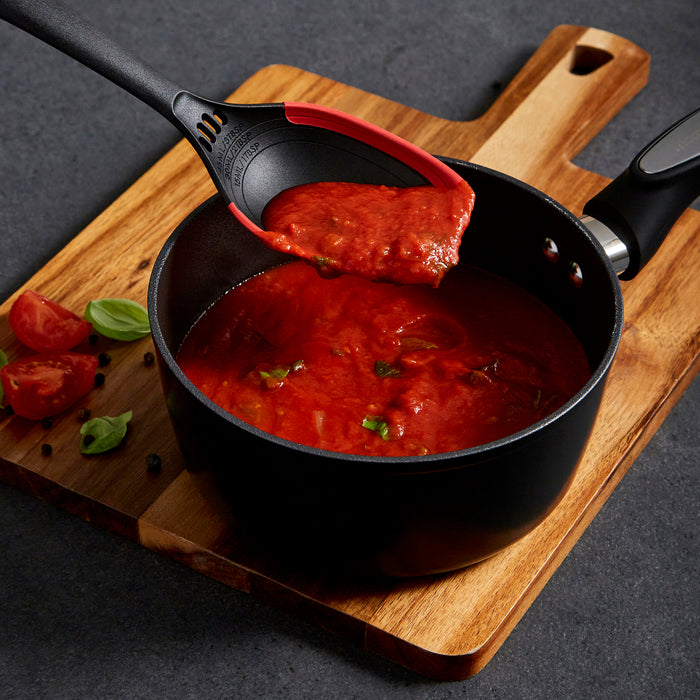Black frying pan with red sauce on a wooden cutting board, surrounded by tomatoes and basil.
