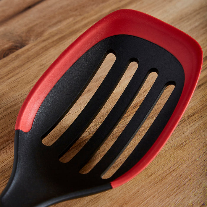 Black and red slotted spatula on a wooden surface