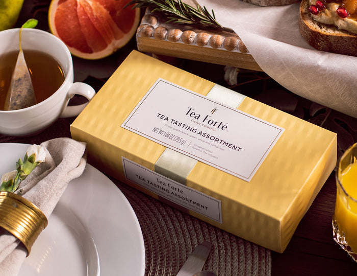 MAIN PDP | Tea Tasting tea assortment in a 10 count petite presentation box with lid closed on dining table with fruit and plate
