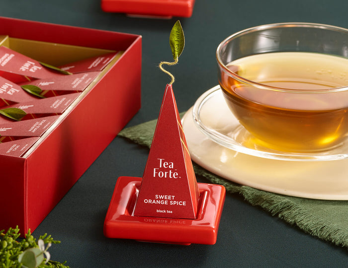 MAIN PDP | Ruby Red Tea Tray with infuser perched on top resting on festive table with cup of tea and Warming Joy Petite Box open