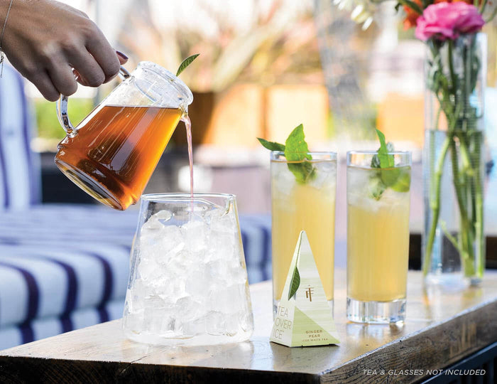 Pouring iced tea into a glass with ice cubes on a table.