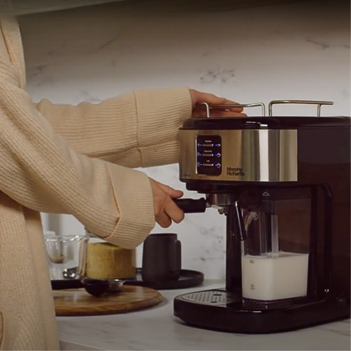 Person using a coffee machine to froth milk in a kitchen setting