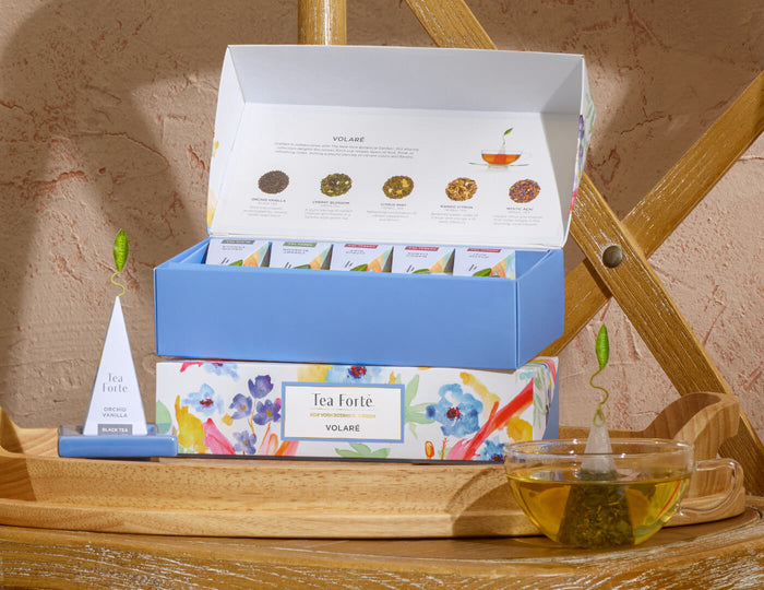 MAIN PDP | Volare Petite Presentation Box, open and closed boxes, stacked on a wooden chair with glass of tea and infuser.