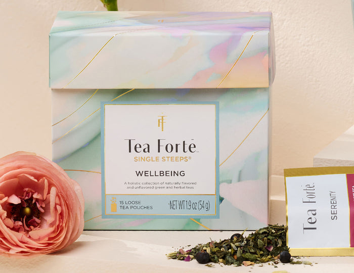 MAIN PDP | Tea Forte Wellbeing Single Steeps Sampler with a pink flower and loose tea leaves on a light background