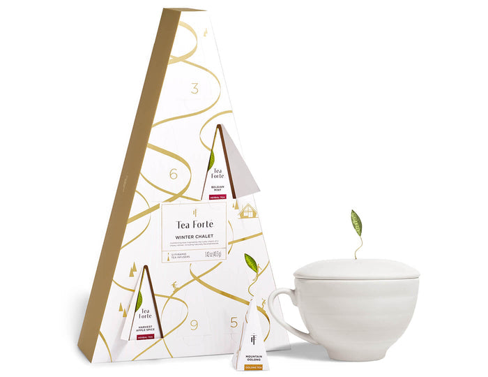 White ceramic teacup with lid and tea bag sachets displayed next to decorative gift box packaging with gold accents.